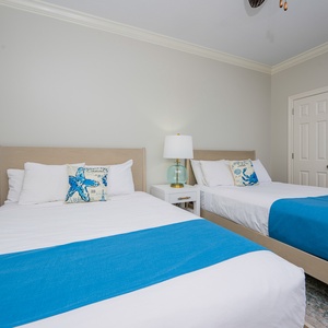 Inviting guest room featuring two cozy queen beds with beach-themed decor and a lamp for a reading light
