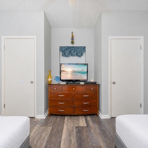 A cozy guest room features two double beds, a wooden dresser with a TV, and a view of a bathroom