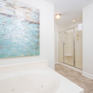 Relax in this serene master bathroom featuring a jetted tub, modern walk-in shower, and calming coastal artwork