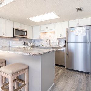 Bright kitchen featuring marbled countertops, white cabinetry, and a breakfast bar with three stools for casual dining
