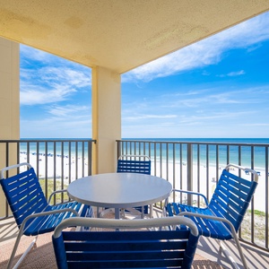 Enjoy a relaxing moment on the balcony with blue seating and a view of the white sand beach and tranquil waters