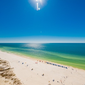This balcony view showcases a bright beach front with soft white sand and vibrant umbrellas, perfect for relaxation