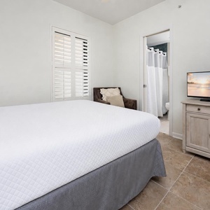 Inviting guest bedroom featuring a queen bed, a cozy chair, and a TV for your entertainment