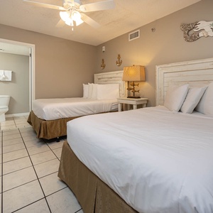 Guest bedroom featuring two double beds with decorative headboards, a bedside lamp, and an adjoining bathroom