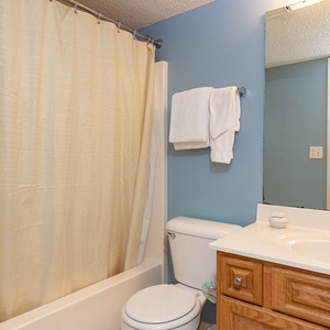 Additional bathroom featuring a tub/shower combo, a wooden vanity, and neatly arranged towels hanging on the wall