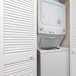 Convenient laundry area featuring a stacked washer and dryer behind stylish white louvered doors for easy access