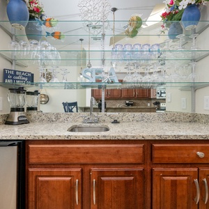 A stylish wet bar area features granite countertops, stainless appliances, and decorative glassware for entertaining