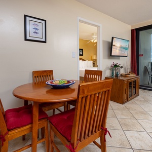 Bright dining area with a wooden table, red cushioned chairs, and a view of the balcony overlooking the serene coastline