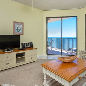 Cozy living area features a TV, floral armchair, and a balcony with a breathtaking view of the tranquil beach