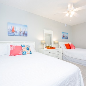 Brightly decorated guest bedroom features two queen beds with nautical artwork, creating a cheerful atmosphere