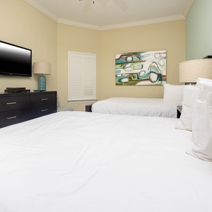 This guest bedroom features two comfortable full beds, a mounted TV, and colorful artwork, creating a welcoming retreat