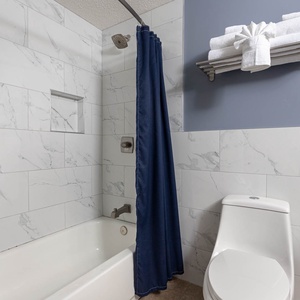 Experience the guest bathroom with elegant tile, a spacious tub-shower, and neatly arranged towels for your convenience