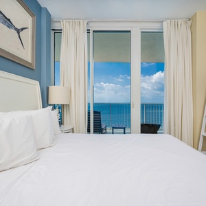 This bedroom features a plush white bed, a TV, and stunning views of the beach from the sliding glass doors