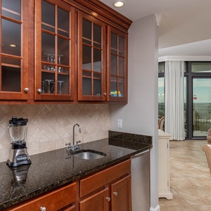 This wet bar features rich wood cabinetry, a sleek granite countertop, blender, and a view of the inviting living area