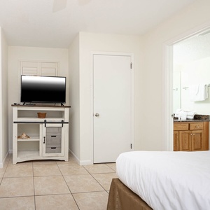 Guest room featuring two double beds, a TV on a white cabinet, and a view into a bathroom with elegant decor and towels