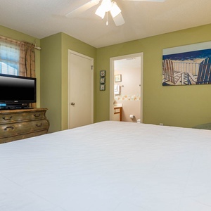 Spacious guest bedroom features a comfortable king bed, a TV on a vintage dresser, and a vibrant beach artwork on the wall