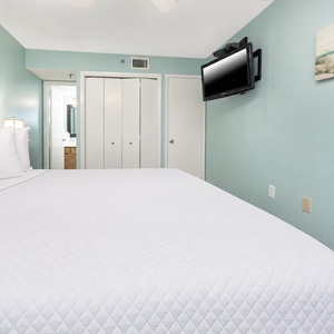 Spacious guest bedroom features a large white king bed, a mounted TV, and soft blue walls, creating a tranquil atmosphere