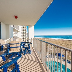 Balcony with blue and beige seating offers a serene view of the gulf and the pool area below, perfect for relaxation