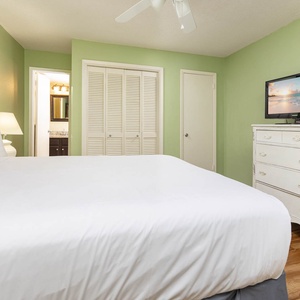 This guest bedroom features a comfortable queen bed, a TV for entertainment, and a calming green color scheme