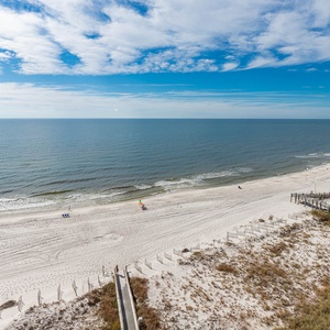 Beach view showcases white sand and gentle waves under a clear blue sky, perfect for relaxation and leisure
