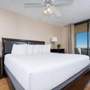 Bright master bedroom featuring a large king bed with plush pillows, a stylish nightstand, and balcony access on the beach