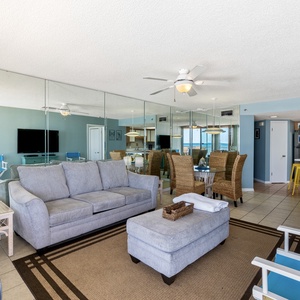 Spacious living area features a comfortable gray sofa, stylish dining set, and a view of the beach through large glass doors