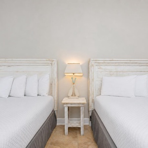 Cozy guest bedroom featuring two white double beds with plush pillows and a charming bedside lamp for a relaxing stay