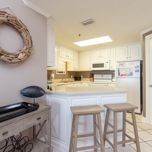 Kitchen area features a breakfast bar with two stools, light cabinetry, and a decorative driftwood wreath on the wall