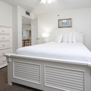 Guest bedroom featuring a cozy queen bed, stylish dresser, and a view of the dining area through the door