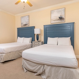 This guest bedroom features two queen beds with blue headboards and soft lighting, perfect for a restful stay