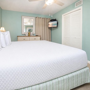 Cozy bedroom featuring a large king bed with white linens, soft blue walls, a TV, and a dresser, creating a serene atmosphere