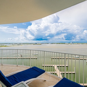 Relax on the balcony's blue loungers while enjoying panoramic views of the tranquil bay and vibrant cloud-filled sky
