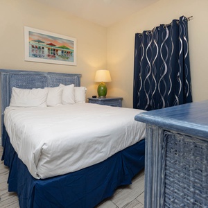 This cozy bedroom features a blue wicker bed frame, colorful artwork, and a TV for relaxing evenings