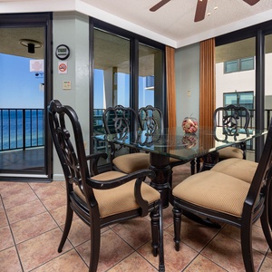 A stylish dining area features a glass table surrounded by elegant chairs, with a stunning view of the beach