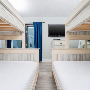This guest bedroom features two cozy bunk beds, a mounted TV, and a bright atmosphere with a view