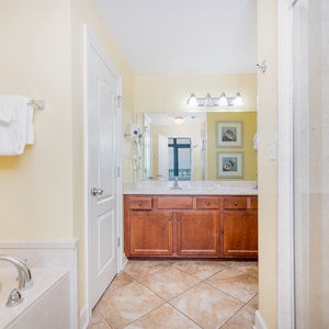 Master bath featuring a jetted tub, walk-in shower, stylish cabinetry, and a large mirror reflecting natural light