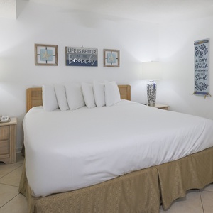 A bright bedroom features a king bed with plush pillows, stylish lamps, and beach decor, creating a relaxing atmosphere