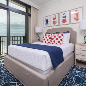 This bedroom features a cozy queen bed with playful polka dot pillows and stunning beachfront views through large glass doors