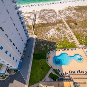 Aerial view of the pool area featuring a mushroom fountain, kiddie pool, lounge chairs, and a pathway leading to the beach