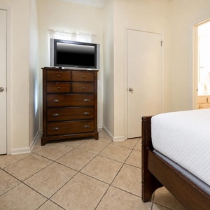 Cozy guest bedroom featuring a wooden dresser with a TV and access to a bright bathroom through a door on the right