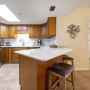 The kitchen features warm wood cabinetry, a breakfast bar with seating, and stainless appliances