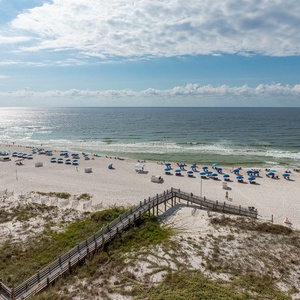A scenic view showcases a wide stretch of white sand beach dotted with blue umbrellas and beachgoers enjoying the sun