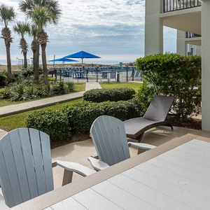 Patio area features a dining table, lounge chairs, and a view of the pool area surrounded by lush greenery and palm trees