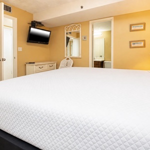 This cozy bedroom features a plush king bed, a mounted TV, and warm yellow walls, creating a relaxing retreat