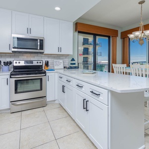 Bright kitchen features white cabinetry, spacious countertop, coffee corner, and a dining area with gulf views