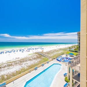 Rows of blue loungers line your pool deck while the coast stretches wide under a clear sky