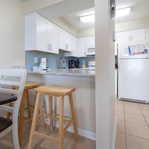 This kitchen features sleek white cabinetry, granite countertops, and a cozy dining area with bar stools for casual meals