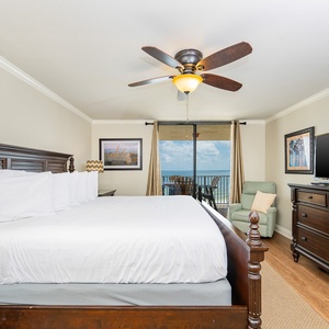 Spacious master bedroom features a king bed, flat-screen TV, and balcony access with a view of the beach and outdoor seating