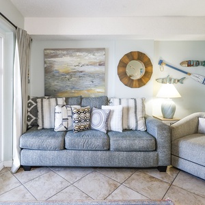 The living area features a sofa with decorative pillows, a warm lamp, and a view of the beach through large sliding doors
