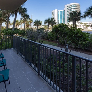 Relax on the guest room balcony with comfortable seating, surrounded by lush greenery and views of the nearby palm trees